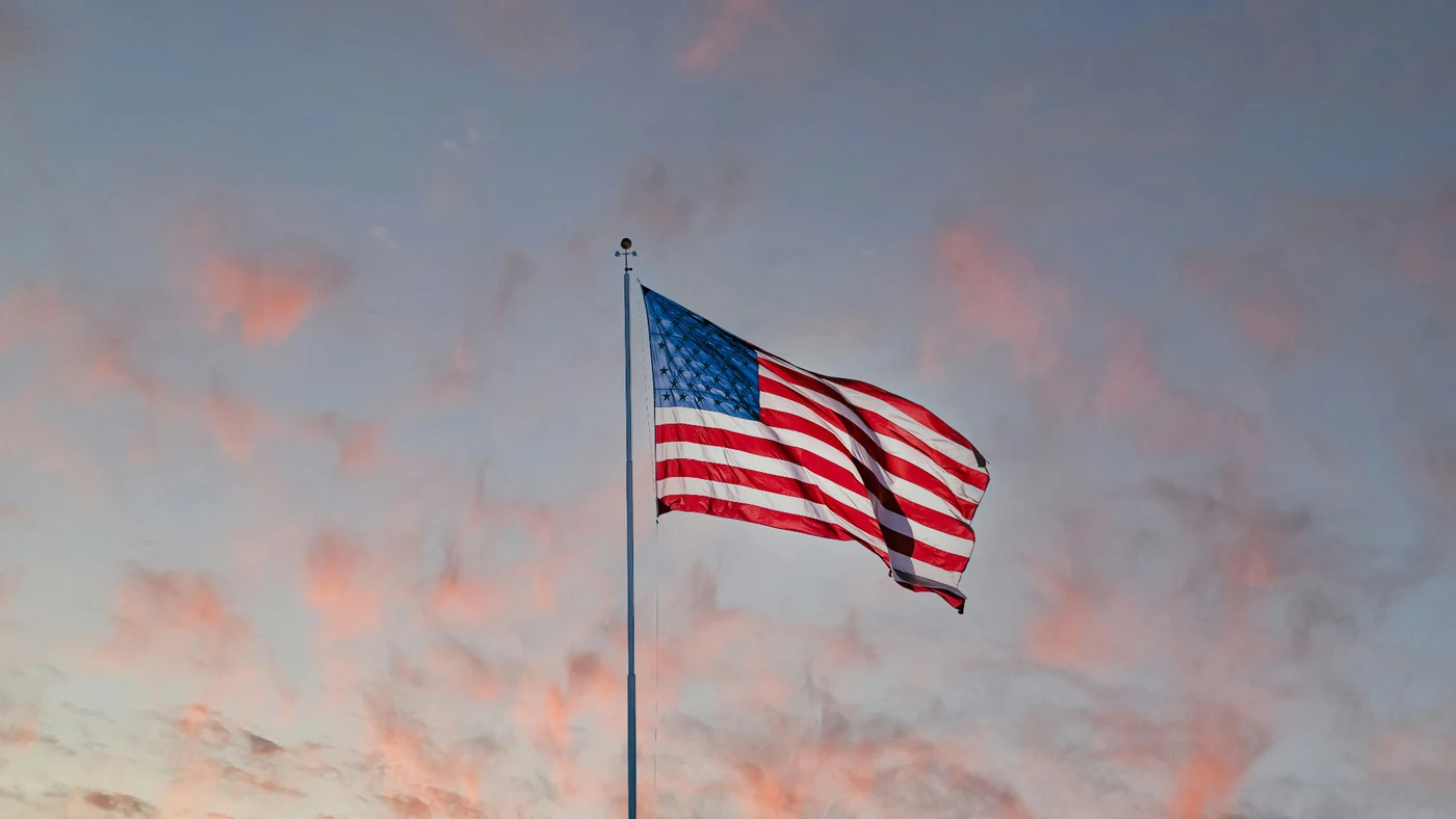 An American flag flying from a flagpole against a softly colored evening sky.